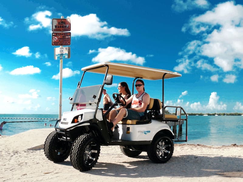 Golf cart rental on Key West beach with two passengers enjoying sunny weather.