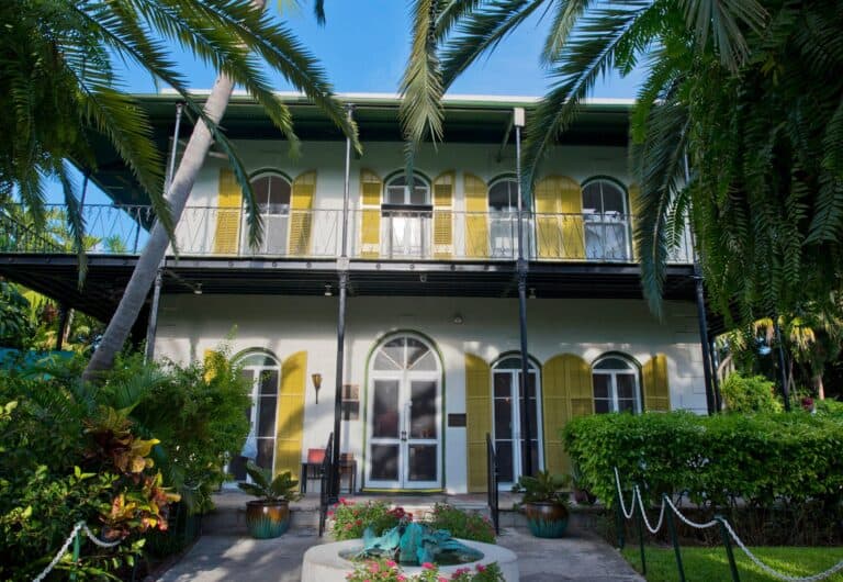 Colorful Key West vacation home with tropical greenery and yellow shutters, perfect for relaxing stays.