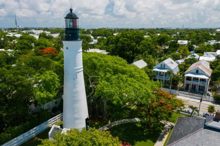 Lighthouse surrounded by lush greenery and historic houses in Key West, Florida.
